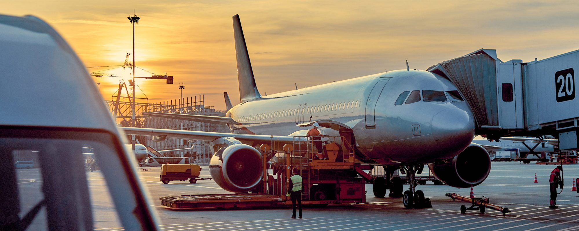 Modern passenger airplane parked to terminal building gate at airside apron of airport with close up airplane parts jet engine wing windows gear tow tractor noon sun view air travel background