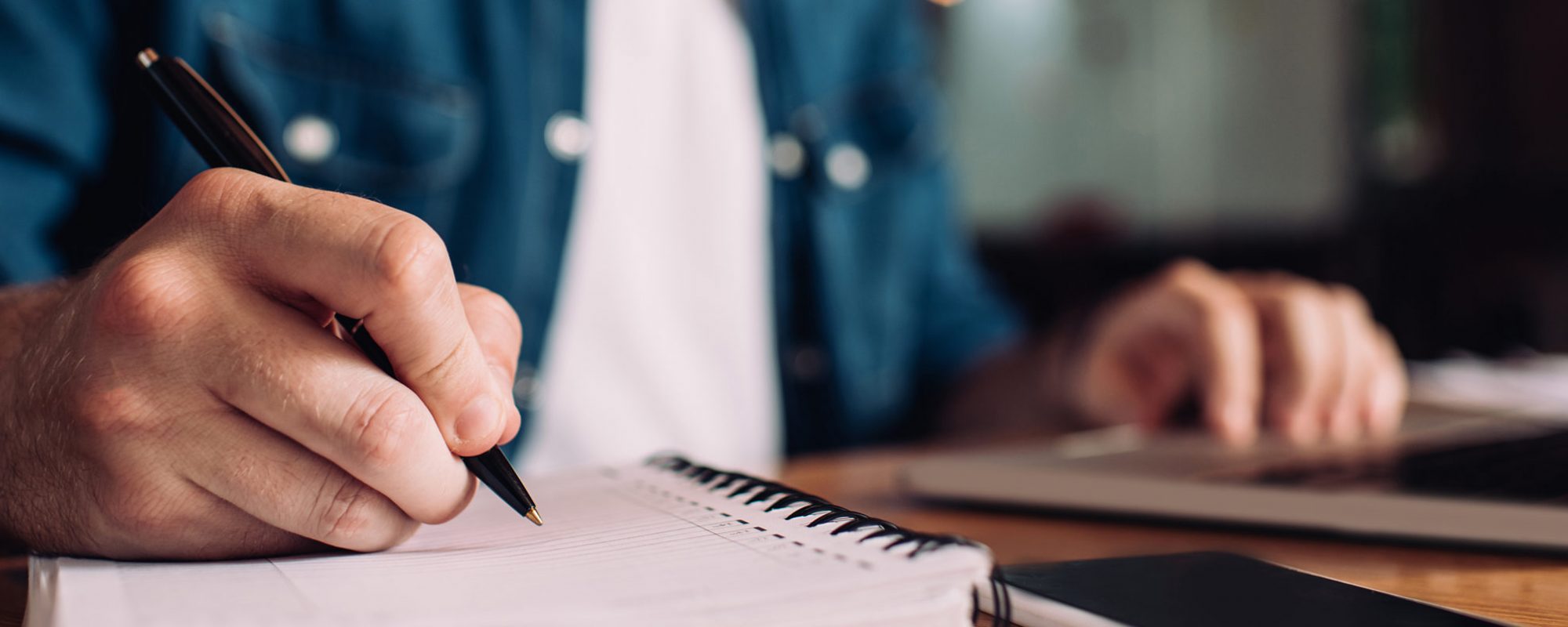 panoramic crop of businessman writing in notebook near smartphone and laptop