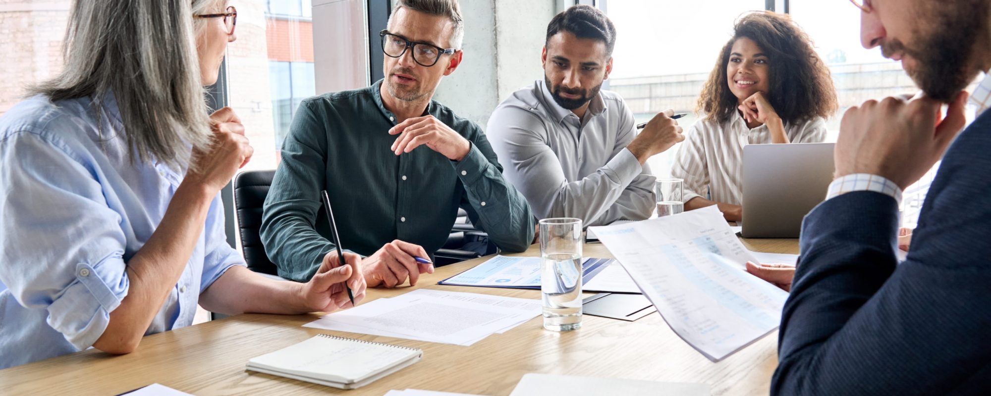 Diverse international executive business partners group discuss report at boardroom meeting table. Multiracial team negotiating project developing business strategy doing paperwork analysis in office.