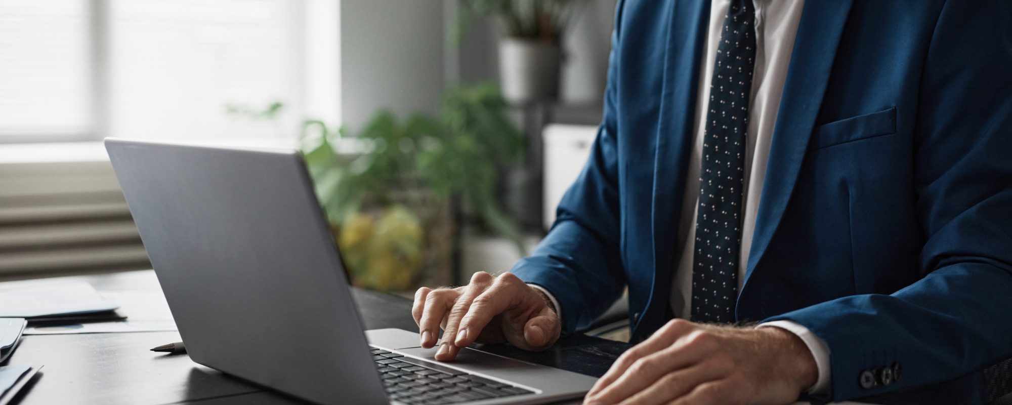 Cropped shot of successful businessman in suit working at able in office and using laptop, copy space