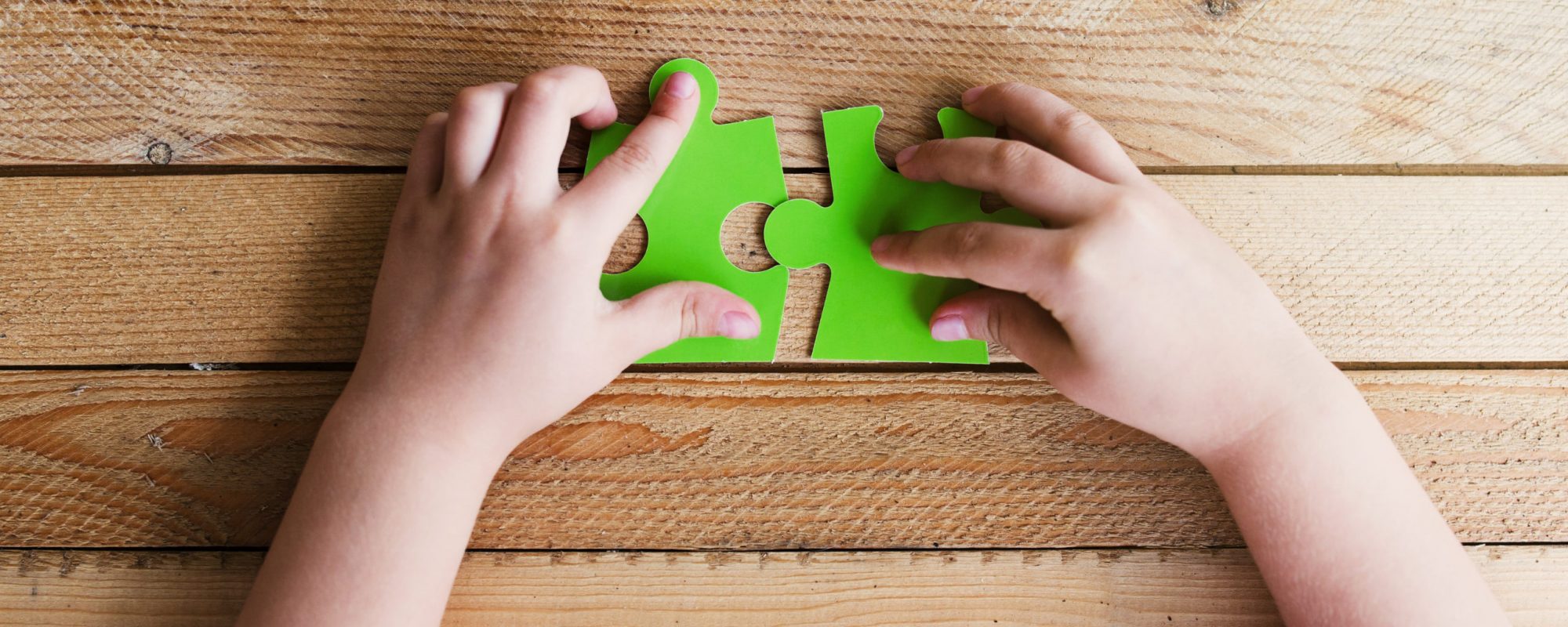 Cropped image of hands connecting two puzzle pieces on wooden table